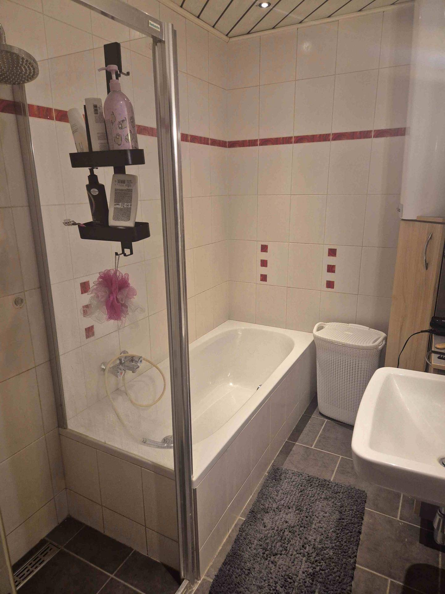 Badezimmer mit Badewanne, Duschabtrennung und Fliesen in Weiß und Rot.