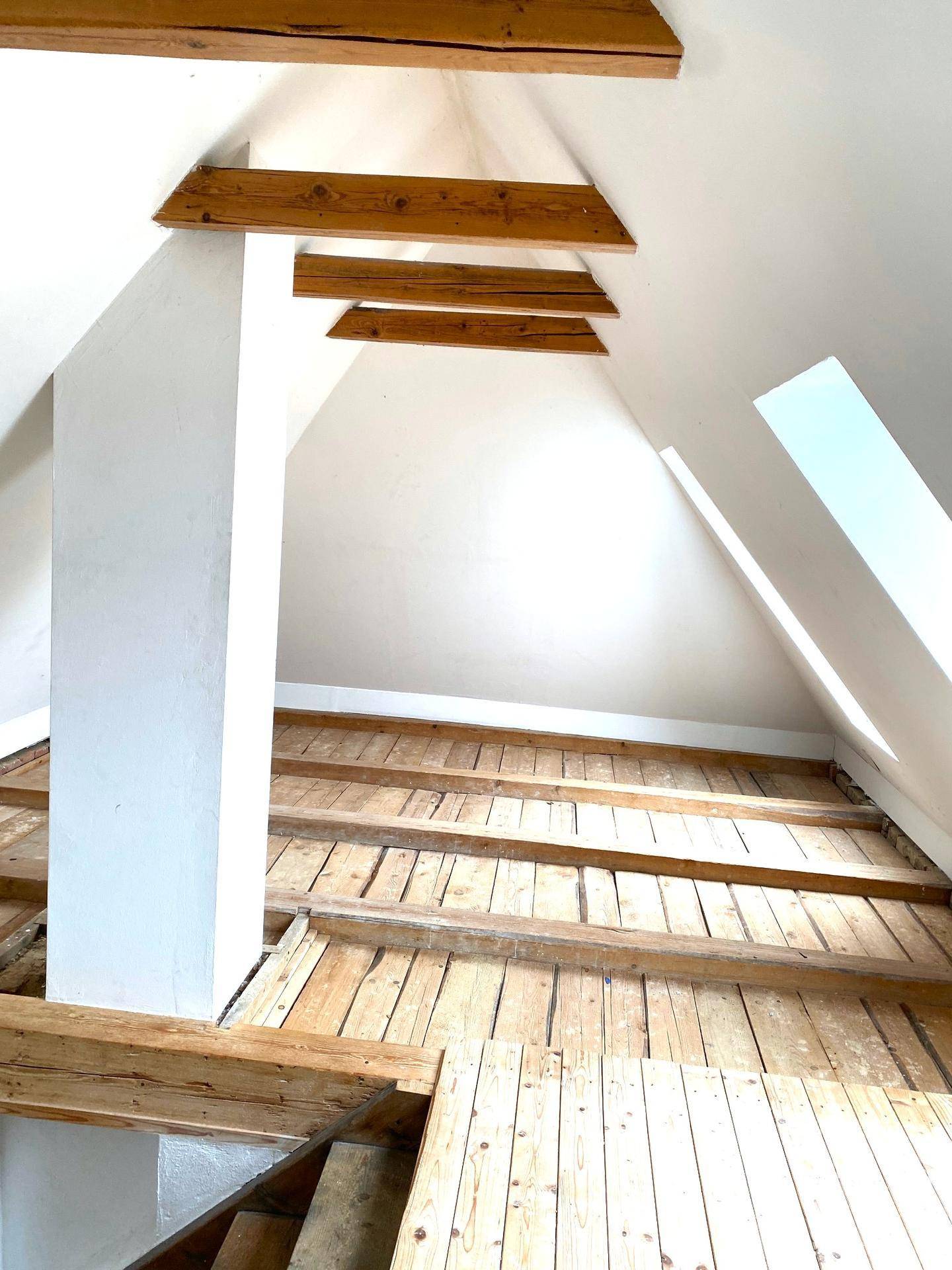 Heller Dachbodenbereich mit sichtbaren Holzbalken und einem Dachfenster.