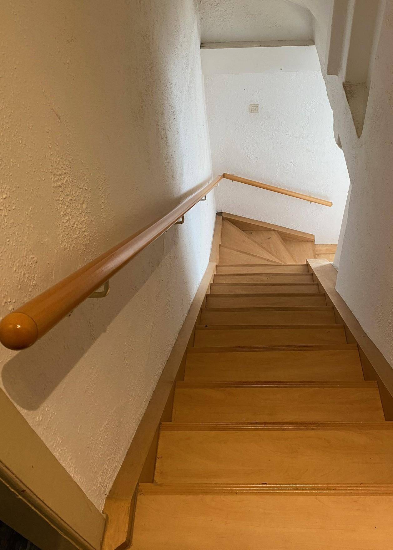 Helles Treppenhaus mit Holzstufen und einem stabilen Holzhandlauf.