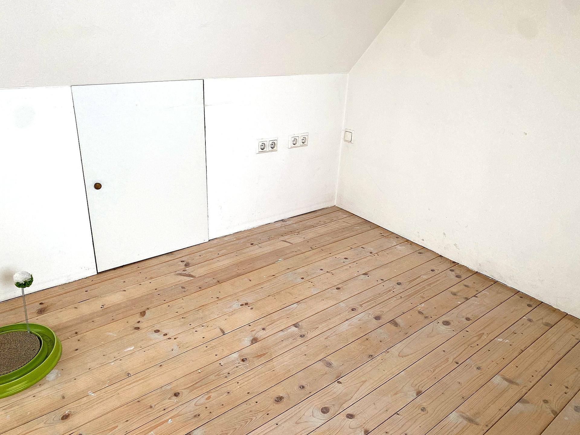 Dachbodenraum mit Holzdielenboden, schrägen Wänden und Stauraumzugang.