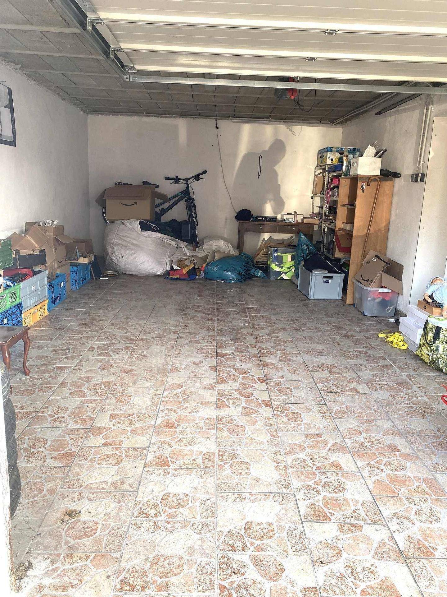 Geräumige Garage mit Fliesenboden und Stauraum für verschiedene Gegenstände.