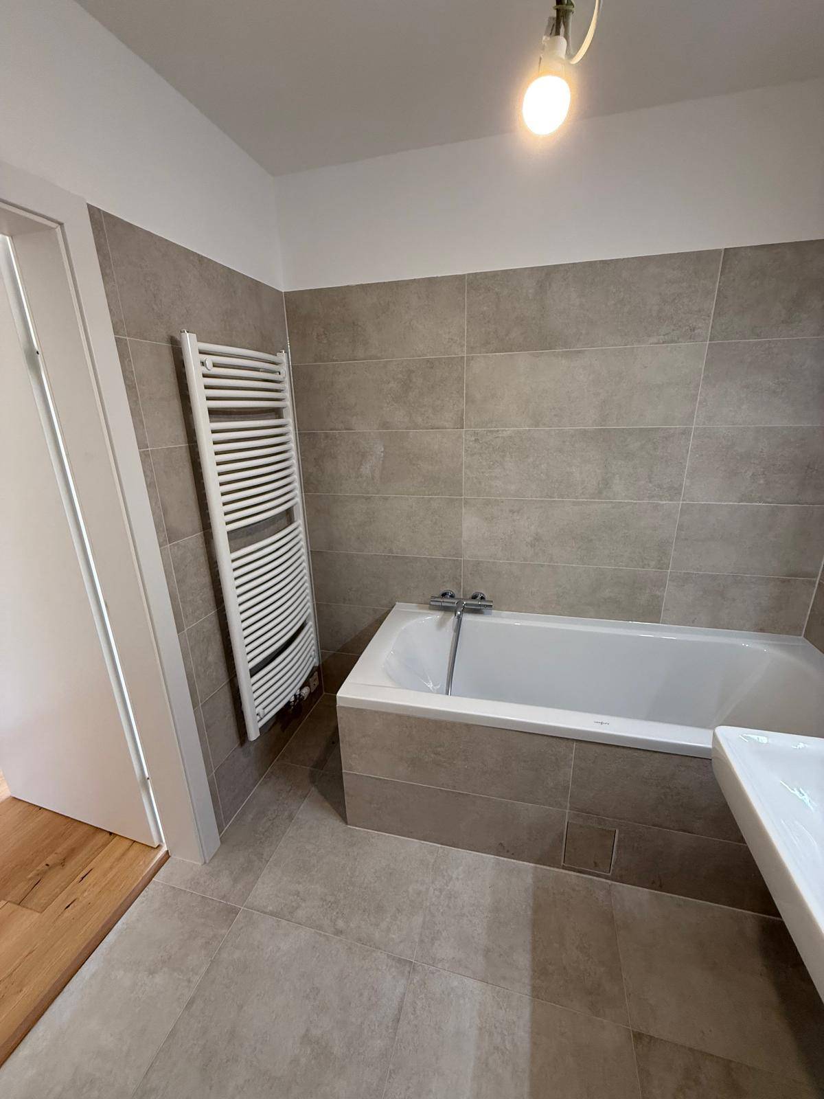 Badezimmer mit Badewanne, beheiztem Handtuchhalter und modernen Fliesen.
