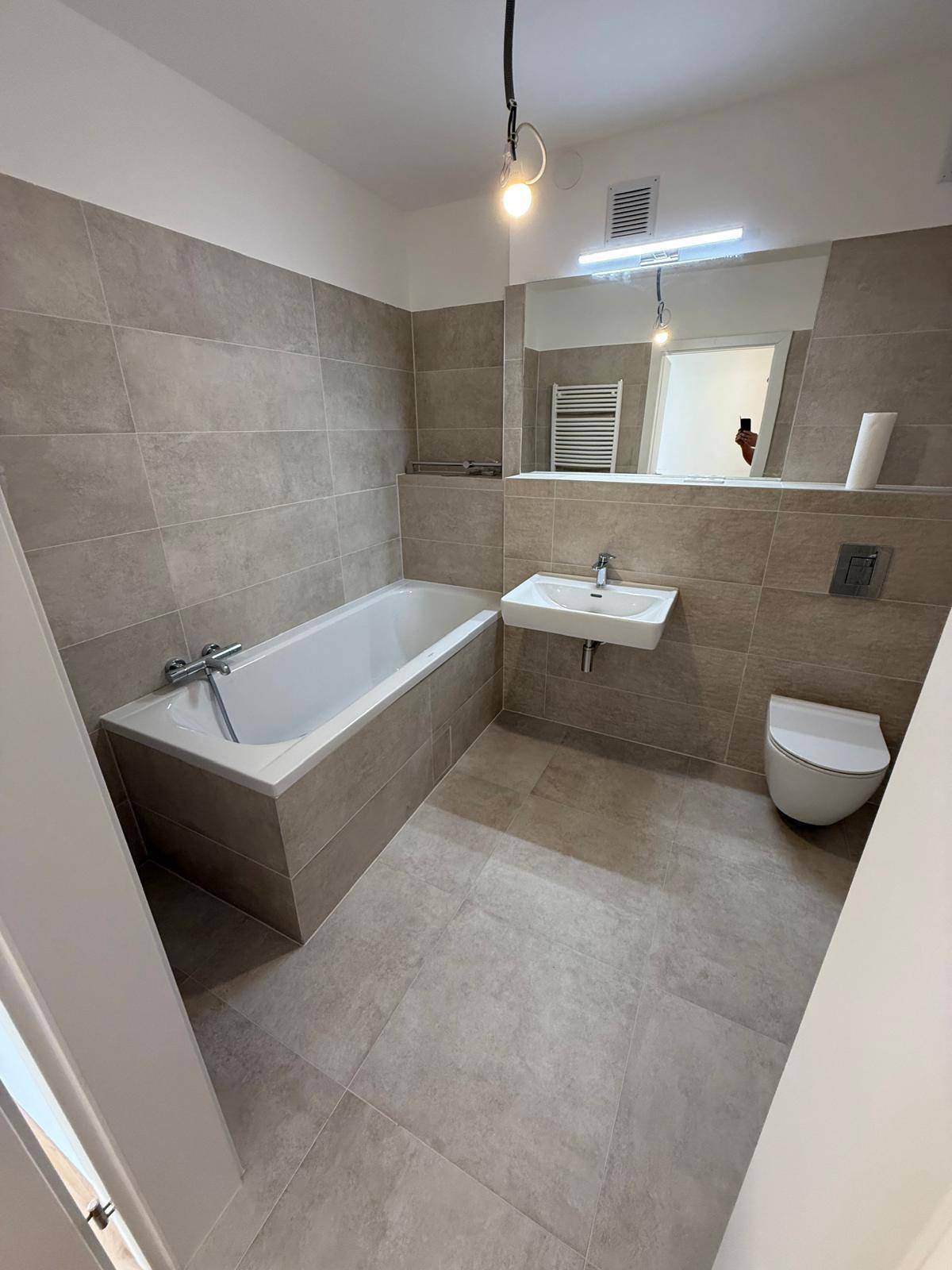 Modernes Badezimmer mit Badewanne, Wand-WC und großformatigen grauen Fliesen.