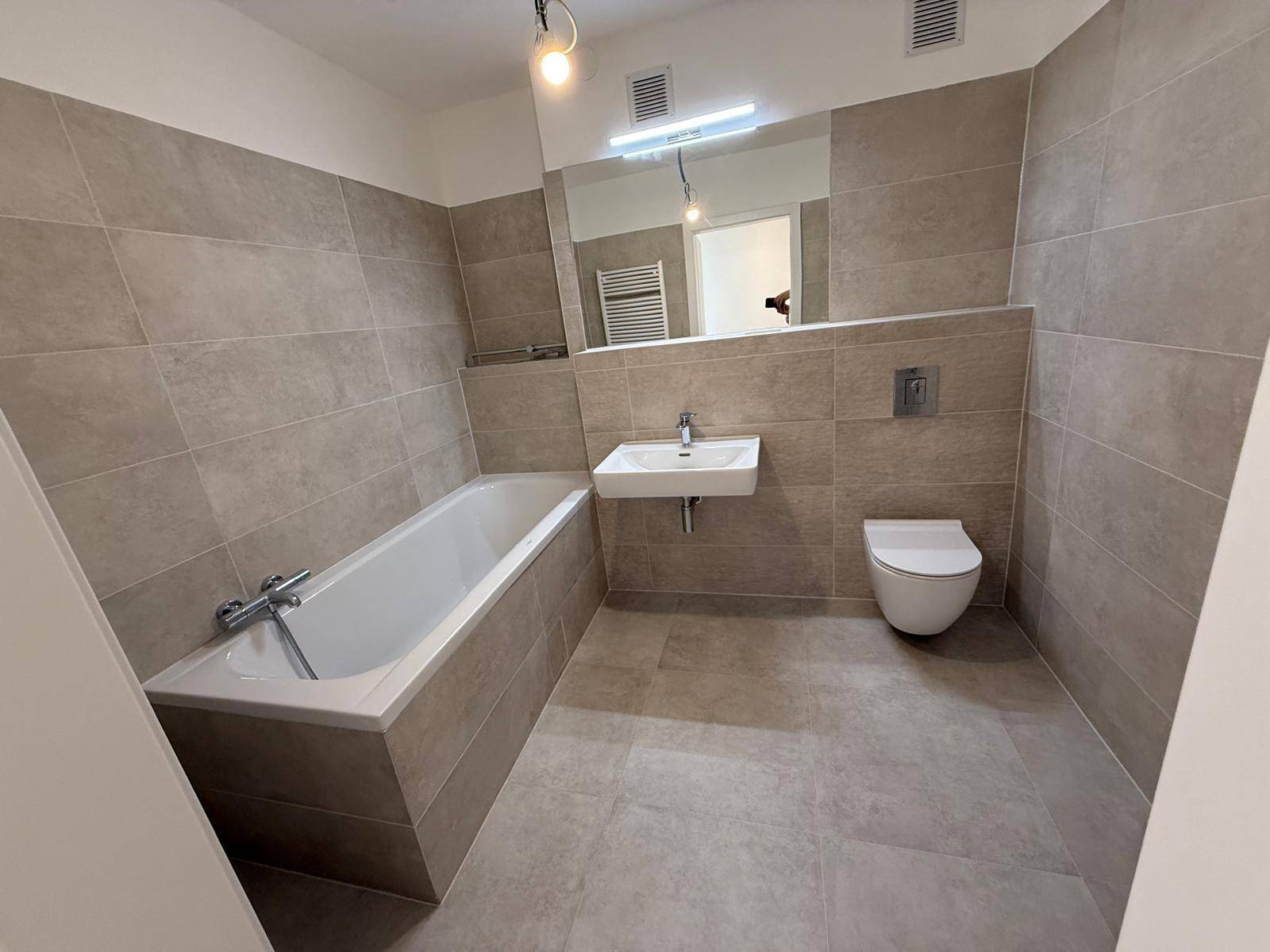 Zeitgemäßes Badezimmer mit Badewanne, Waschbecken und WC, ausgestattet mit hellgrauen Fliesen.