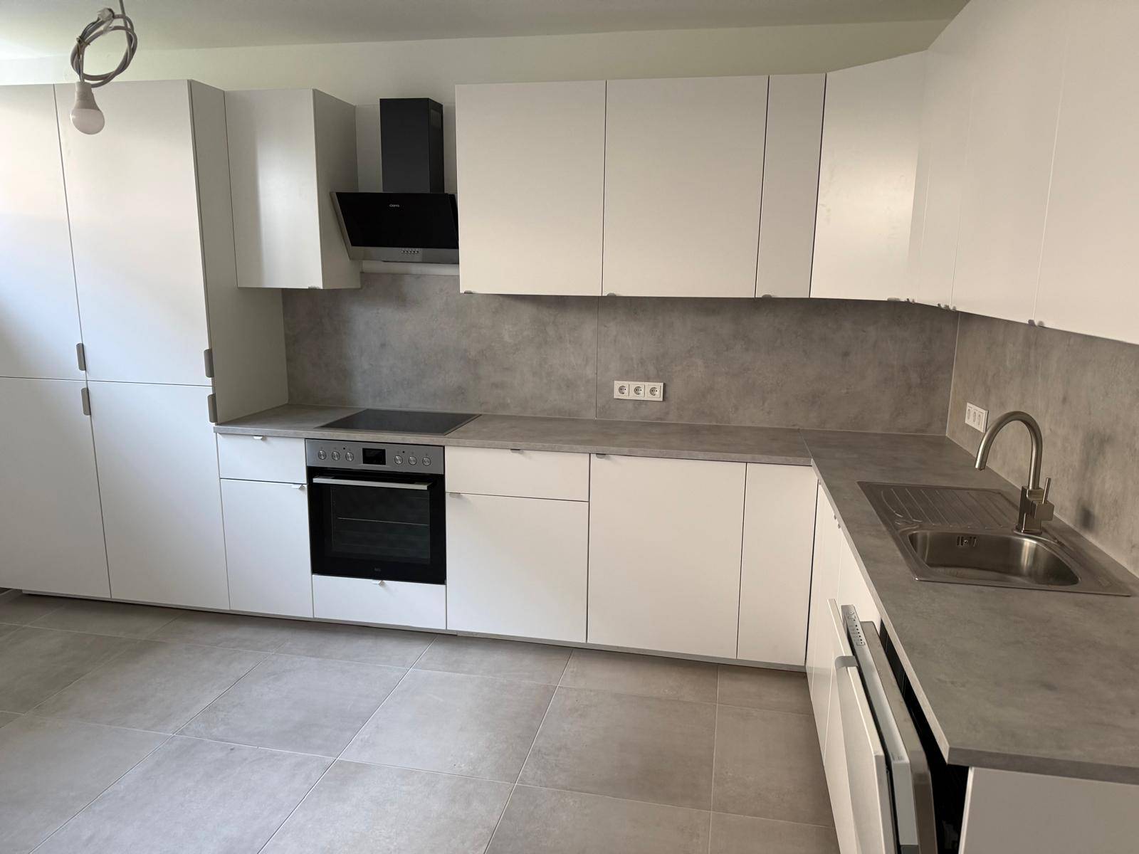 Neue Küche mit weißen Fronten, integriertem Backofen und Induktionskochfeld, bereit zur Nutzung.