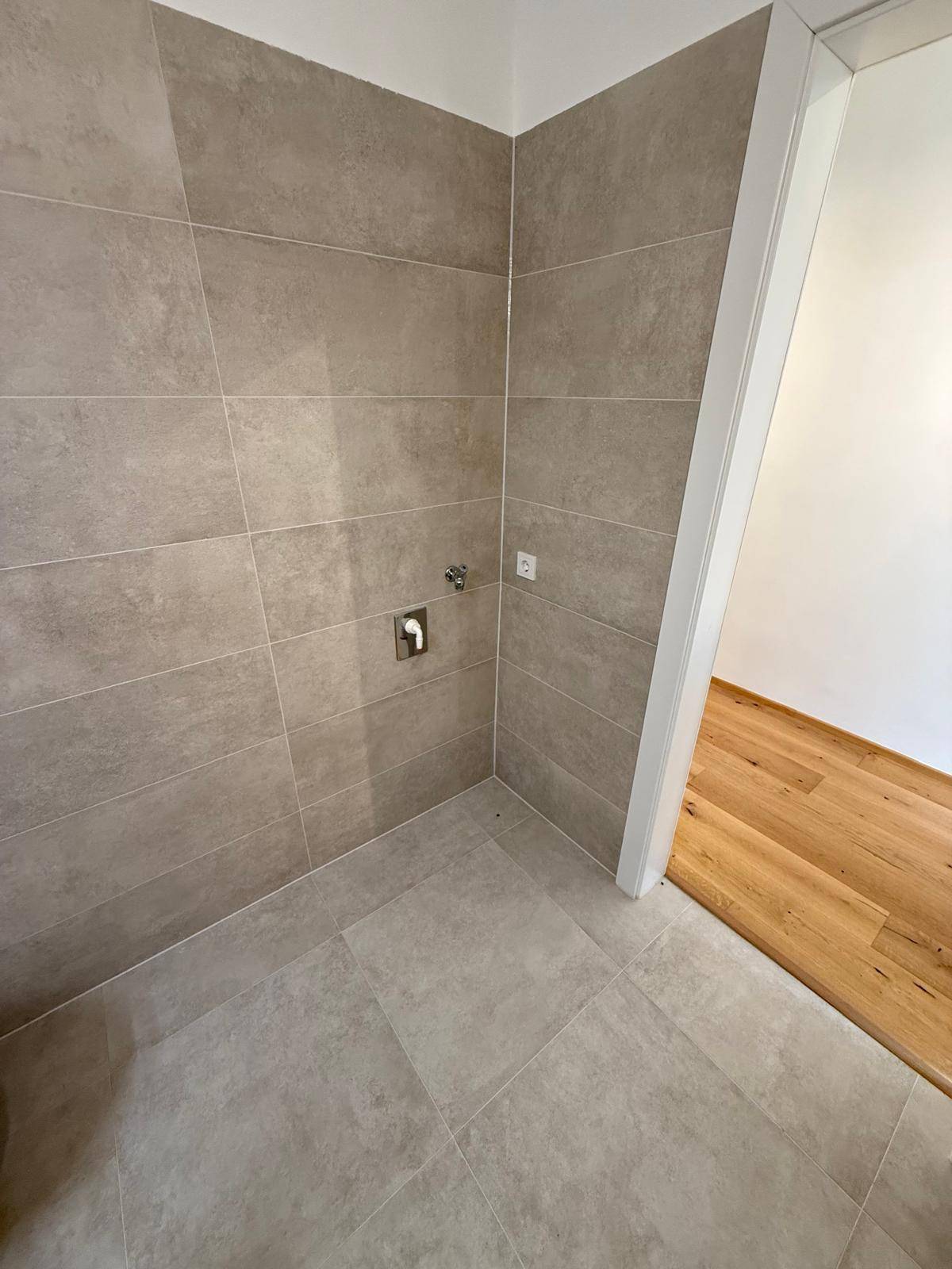 Gefliester Bereich im Badezimmer, vorbereitet für eine Dusche oder Waschmaschine.