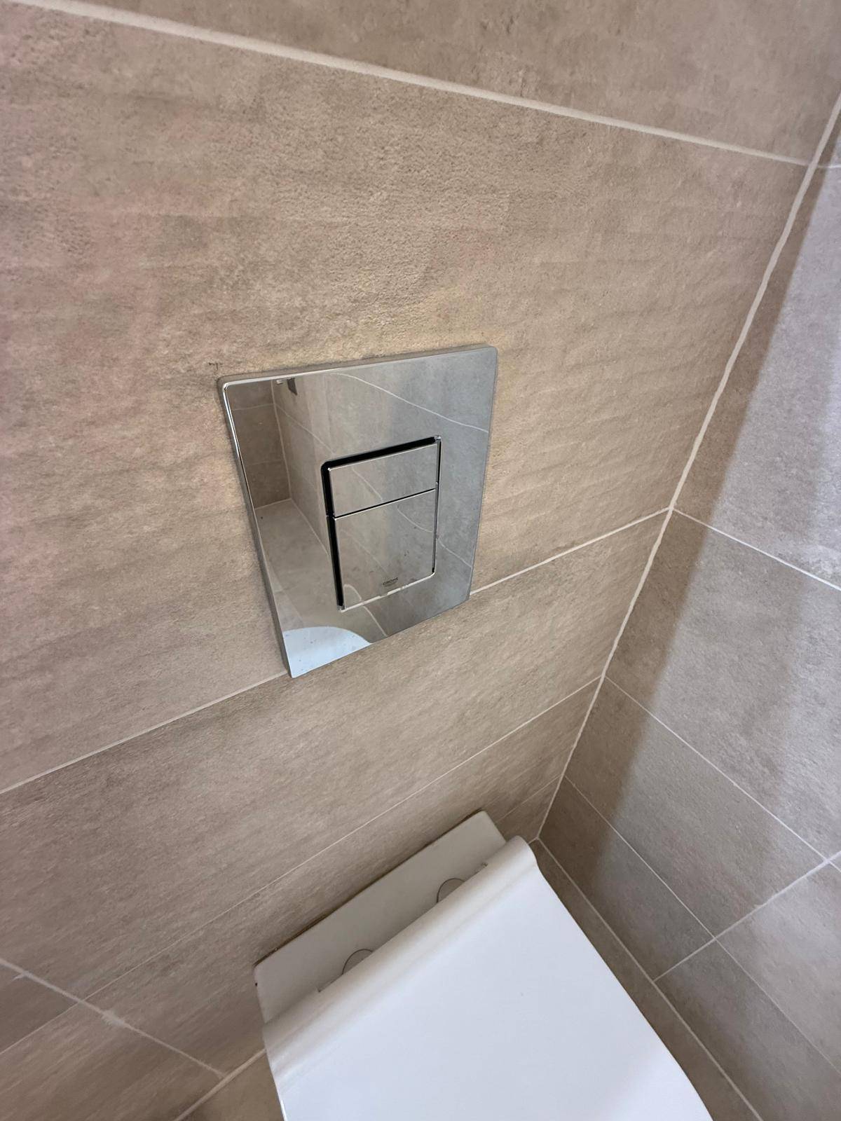 Moderner Spülkasten mit Chrom-Finish an der gefliesten Wand des Badezimmers.
