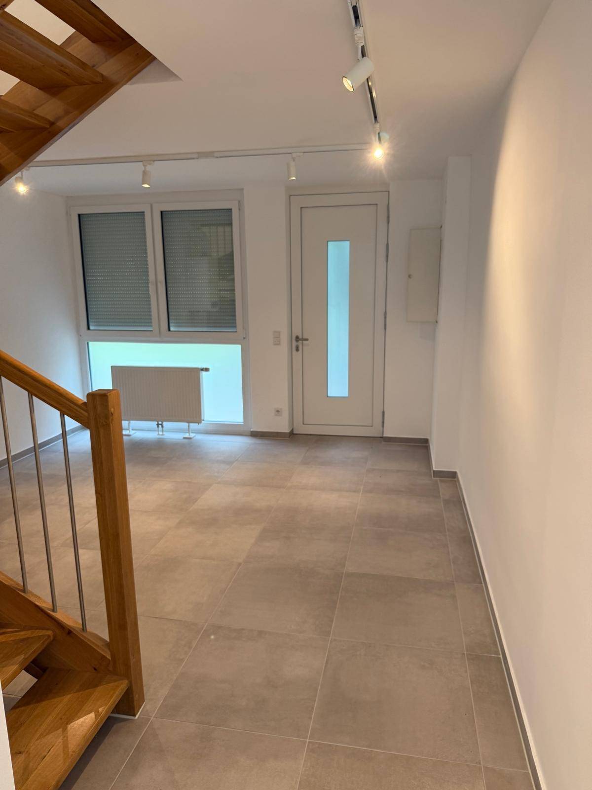 Eingangsbereich mit Fliesenboden, Holztreppe und einer modernen Eingangstür.