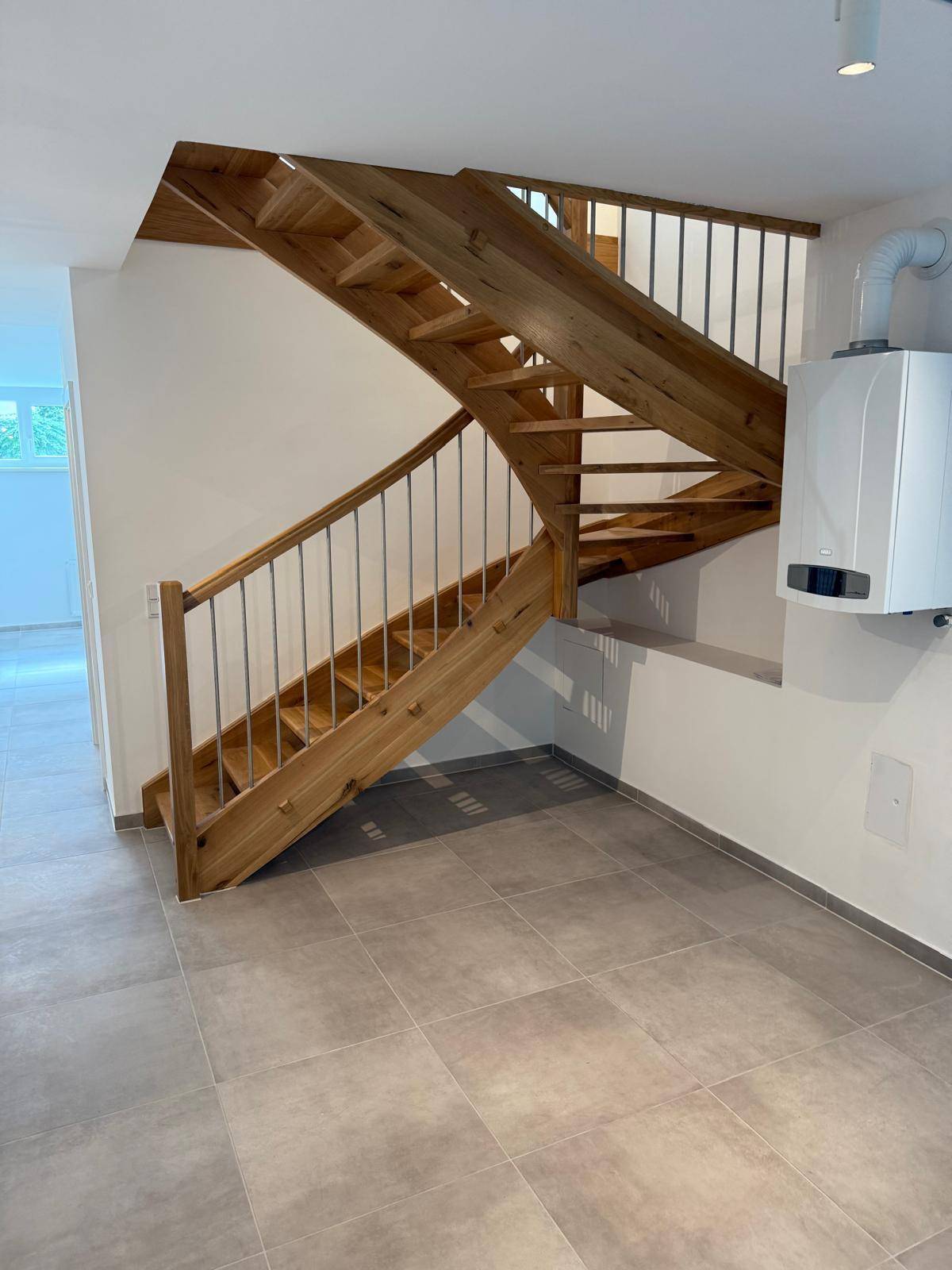 Offener Bereich mit Holztreppe, Fliesenboden und einem Heizkessel an der Wand.