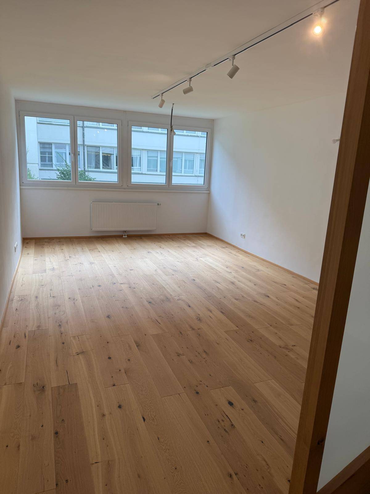 Geräumiger Wohnbereich mit Holzboden und großen Fenstern, die den Raum erhellen.