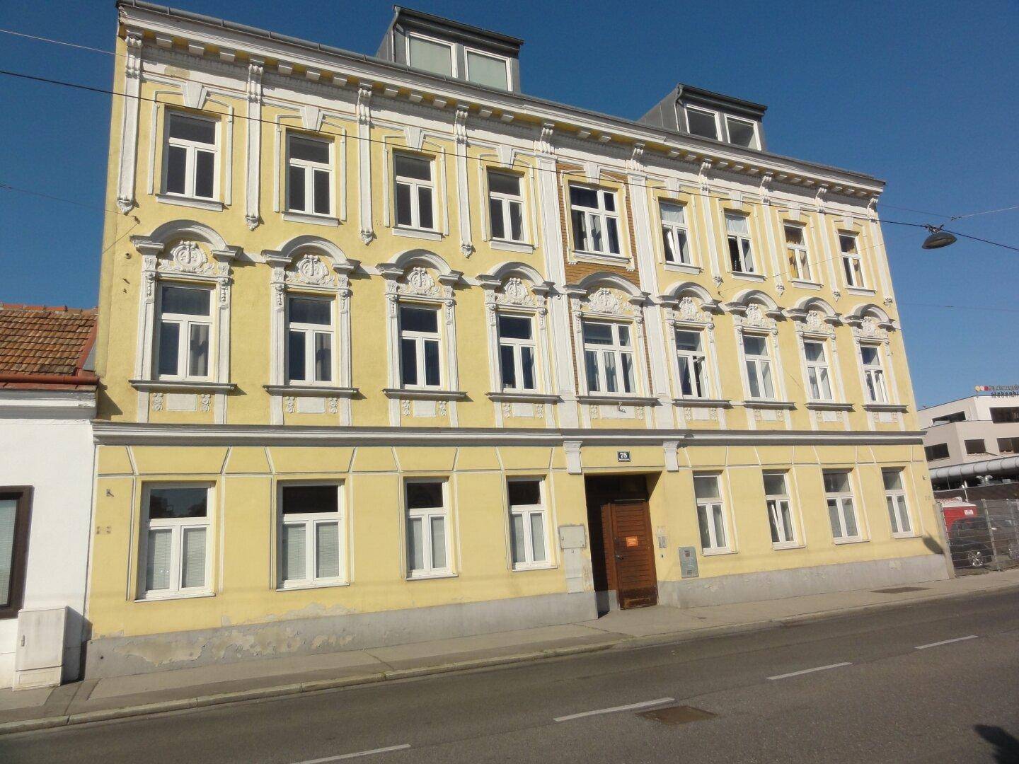 Historische gelbe Fassade eines Altbaus mit vielen Fenstern und dekorativen architektonischen Elementen.