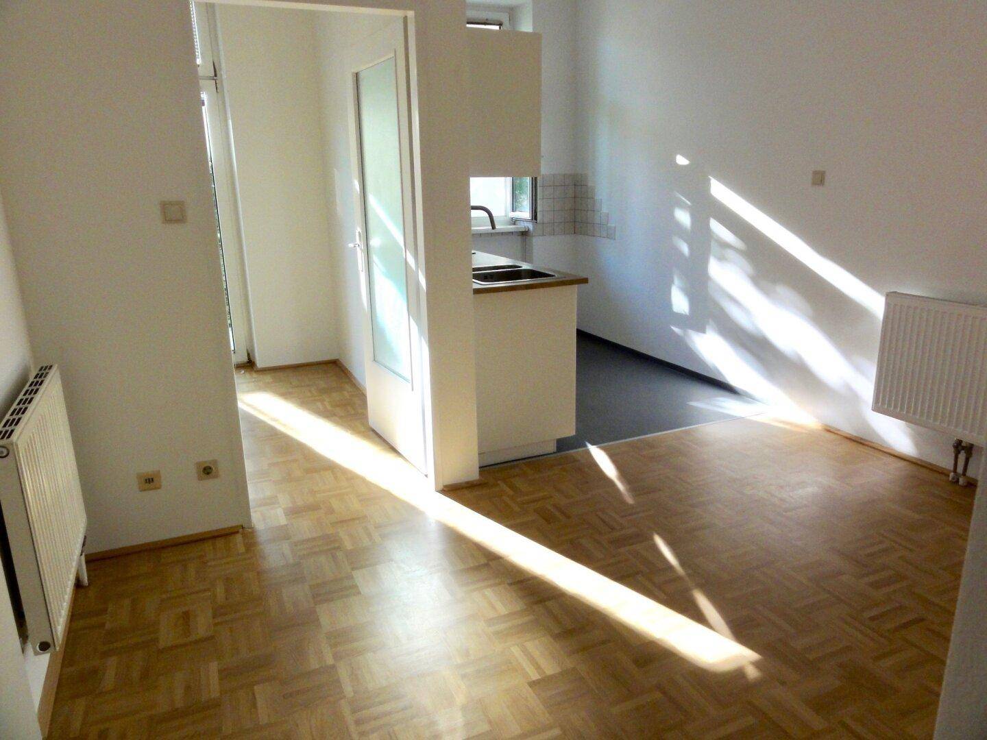 Lichtdurchfluteter Wohnbereich mit Parkettboden und Übergang zu einer halboffenen Küche.