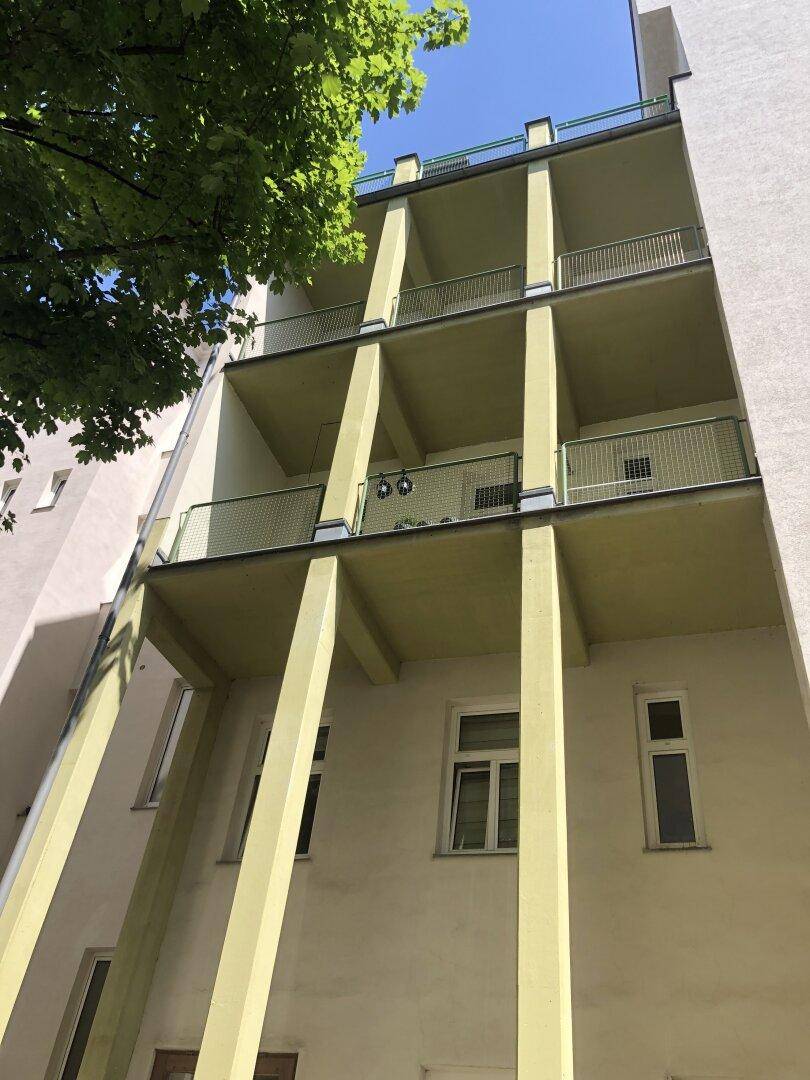 Rückfassade des Gebäudes mit mehreren übereinanderliegenden Balkonen und grünen Säulen.