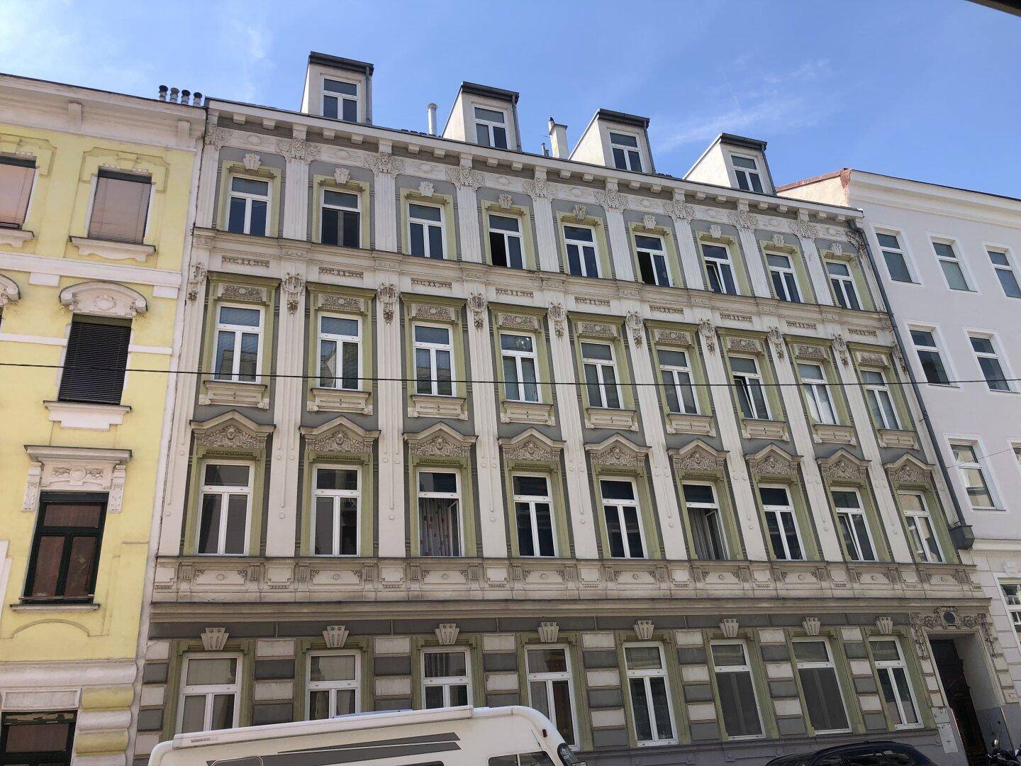 Historische Fassade eines Altbaus mit reich verzierten Fenstern und architektonischen Details.
