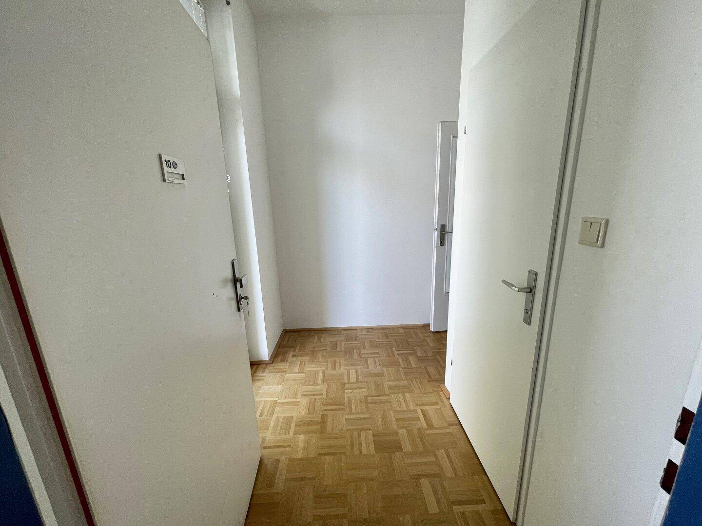 Heller Flur mit Parkettboden und mehreren weißen Türen, die zu den Zimmern führen.