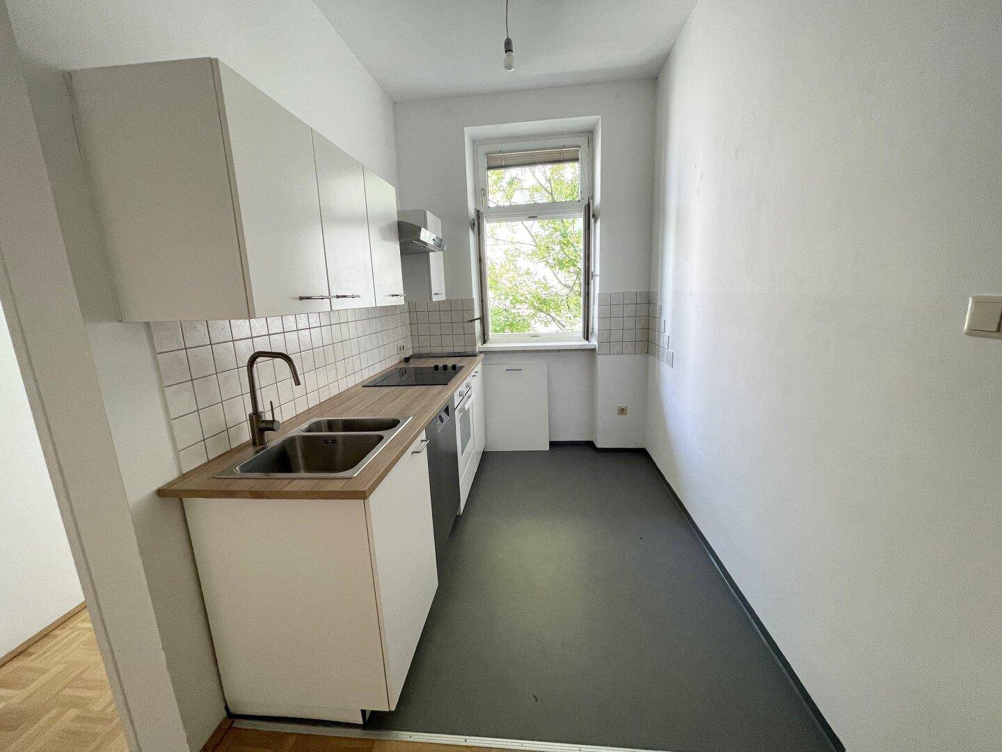 Funktionale, schmale Küche mit weißen Schränken, Kochfeld und Fenster für Tageslicht.