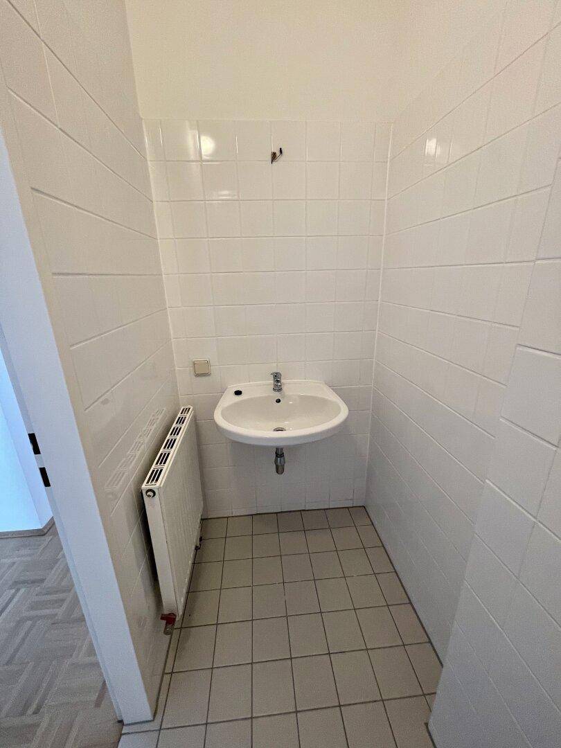 Badezimmer mit einem einzelnen Waschbecken und weißen Wandfliesen, hell und gepflegt.