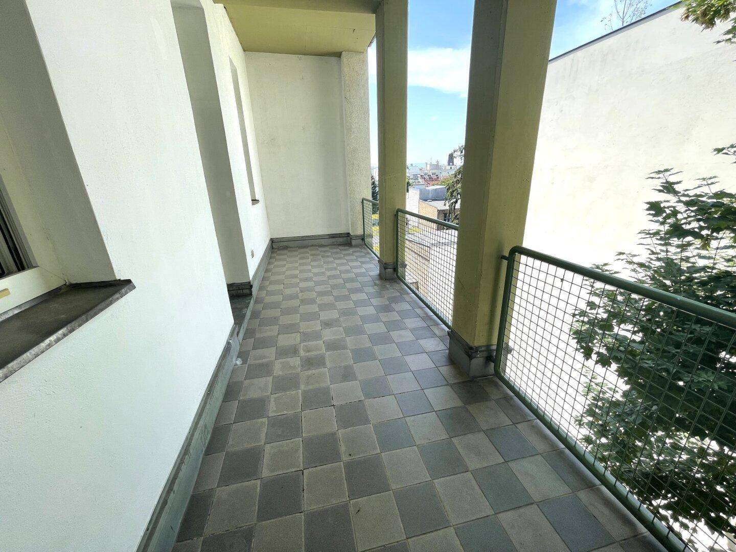 Heller Balkon mit kariertem Fliesenboden und weitem Blick über die Stadt und grüne Bäume.
