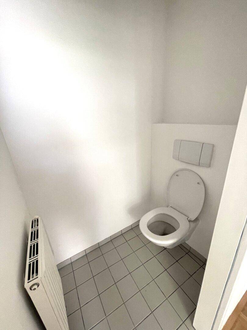 Separates WC mit wandhängender Toilette und hellen Bodenfliesen, praktisch und platzsparend.