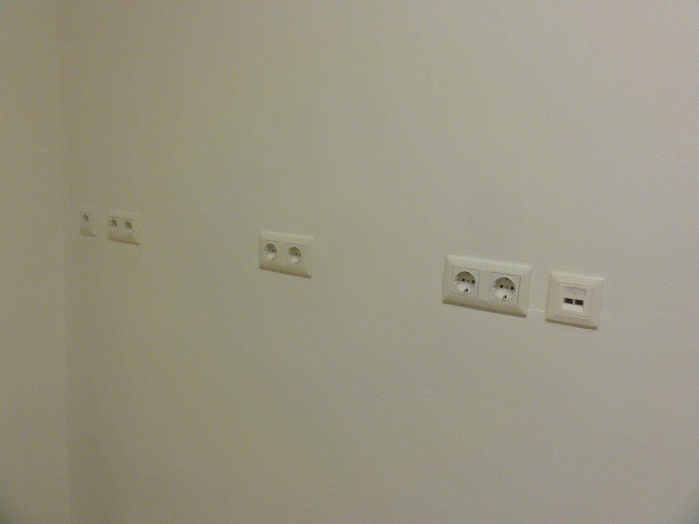 Nahaufnahme einer weißen Wand mit mehreren Steckdosen und Schaltern.