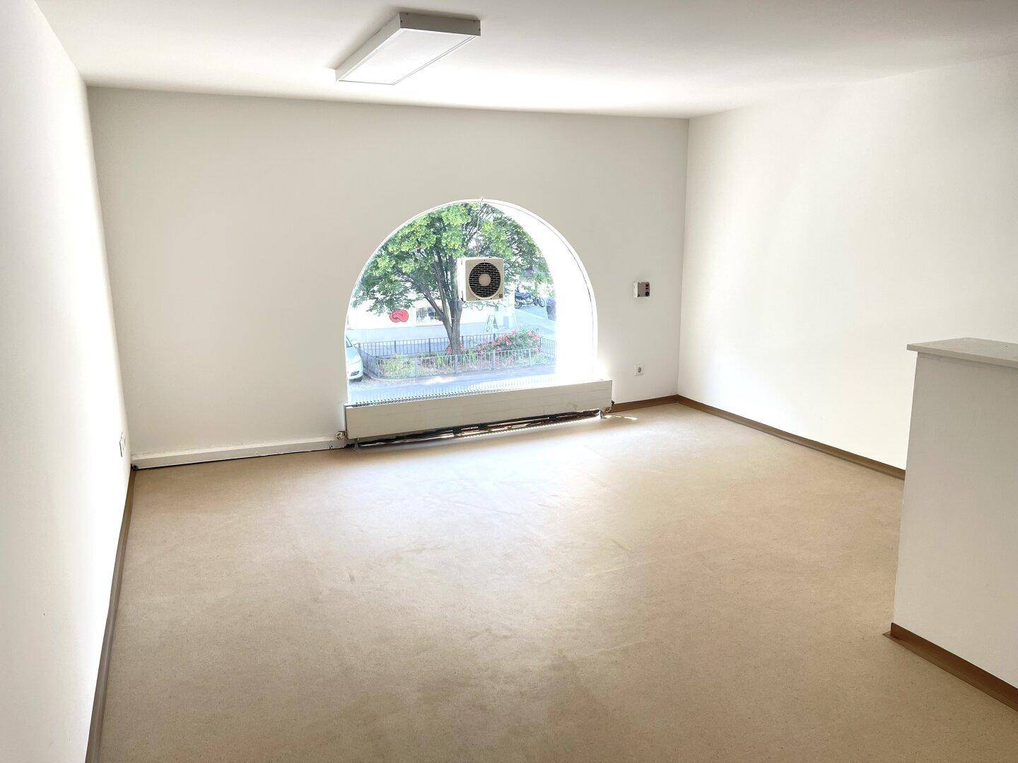 Heller Raum mit großem Rundbogenfenster und Linoleumboden, vielseitig nutzbar.