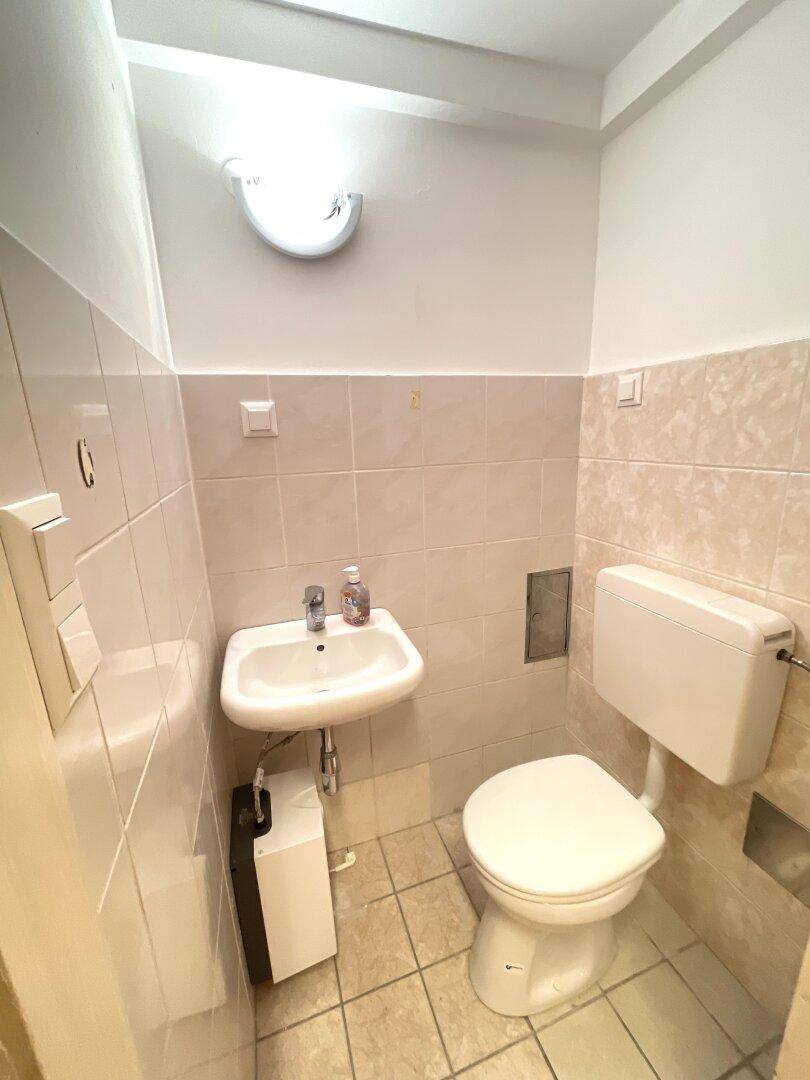 Toilette mit Waschbecken und Fliesen an Wänden und Boden, in neutralen Farbtönen.