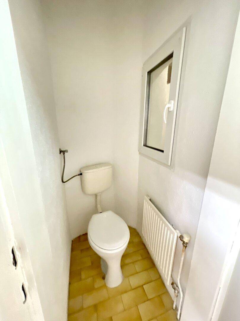 Einfache Toilette mit Fenster und Heizkörper, in einem kleinen, hellen Raum.