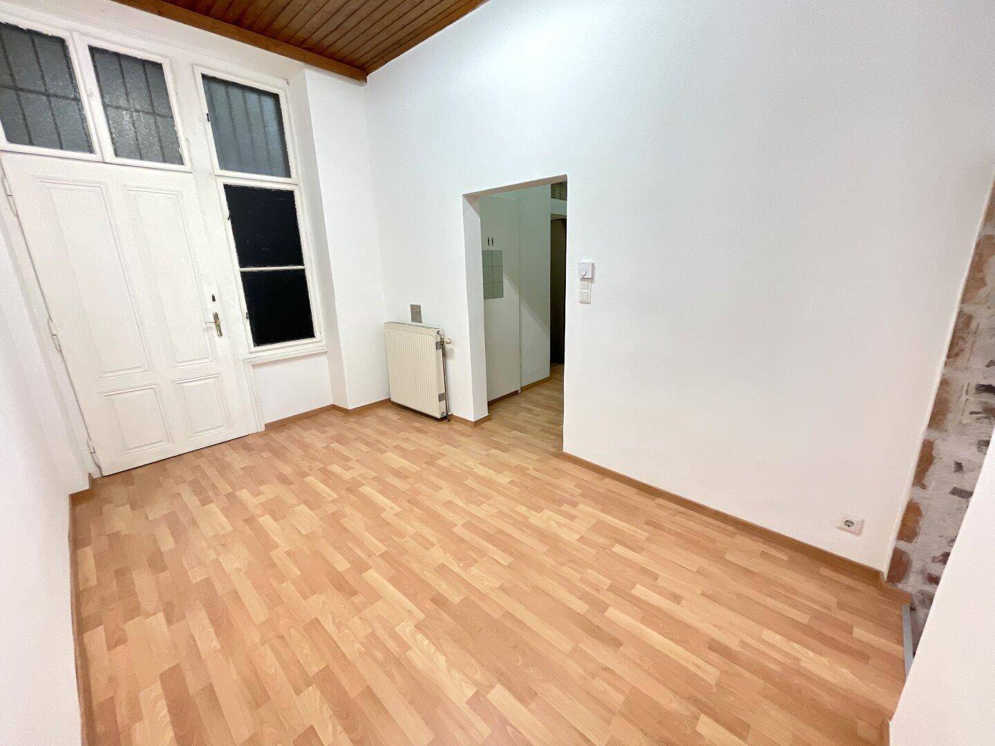 Raum mit Holzboden, Holzbalkendecke und hohen Fenstertüren, die viel Licht spenden.