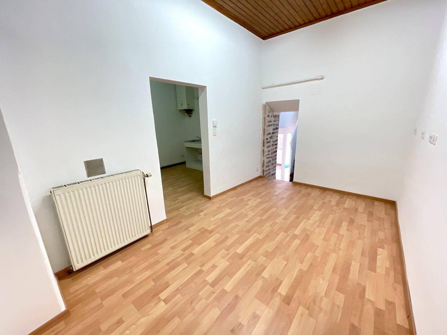 Heller Raum mit Holzboden und Holzbalkendecke, mit Zugang zu einem Nebenraum.