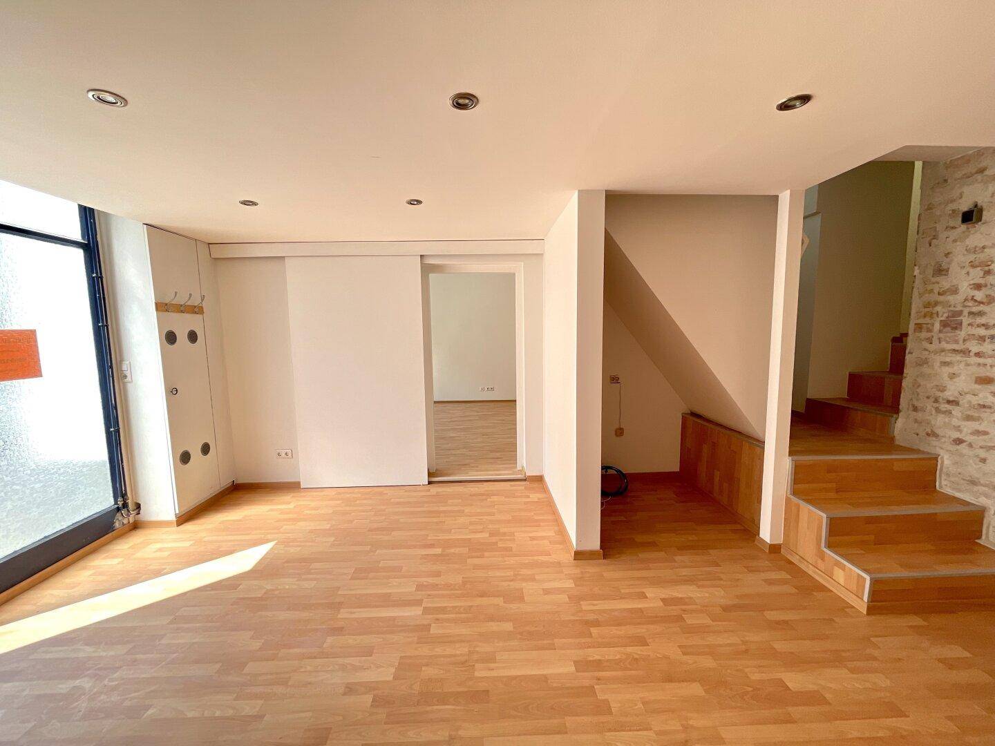 Heller Raum mit Holzboden, Schiebetür und Treppenaufgang, ideal für flexible Nutzung.