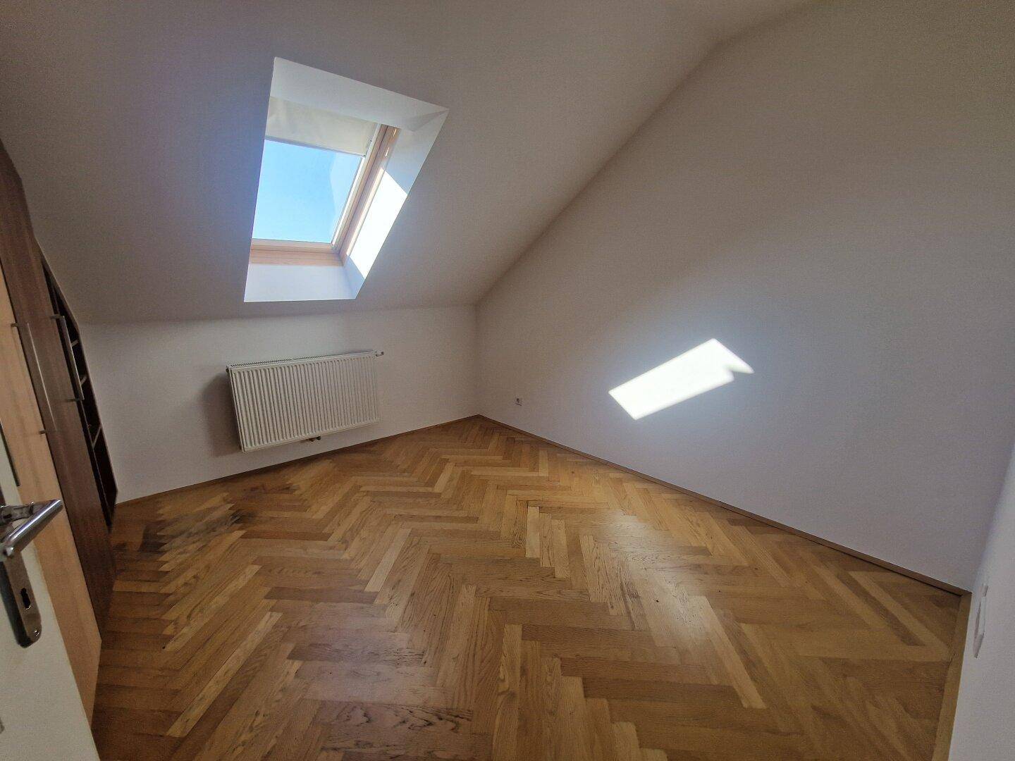 Gemütliches Schlafzimmer mit Fischgrätparkett und einem Dachfenster, das für angenehmes Tageslicht sorgt.