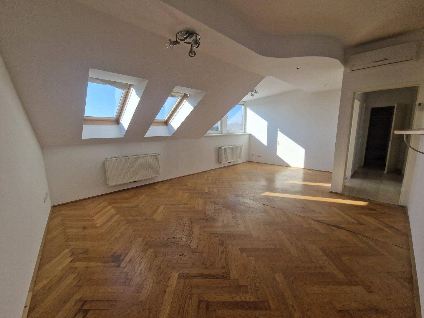Helles Wohnzimmer mit Fischgrätparkett, Dachschrägen und mehreren Dachfenstern, die viel Tageslicht hereinlassen.