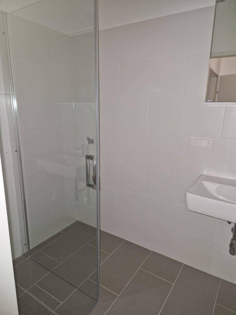 Helles Badezimmer mit begehbarer Dusche, modernem Waschbecken und weißen Wandfliesen.