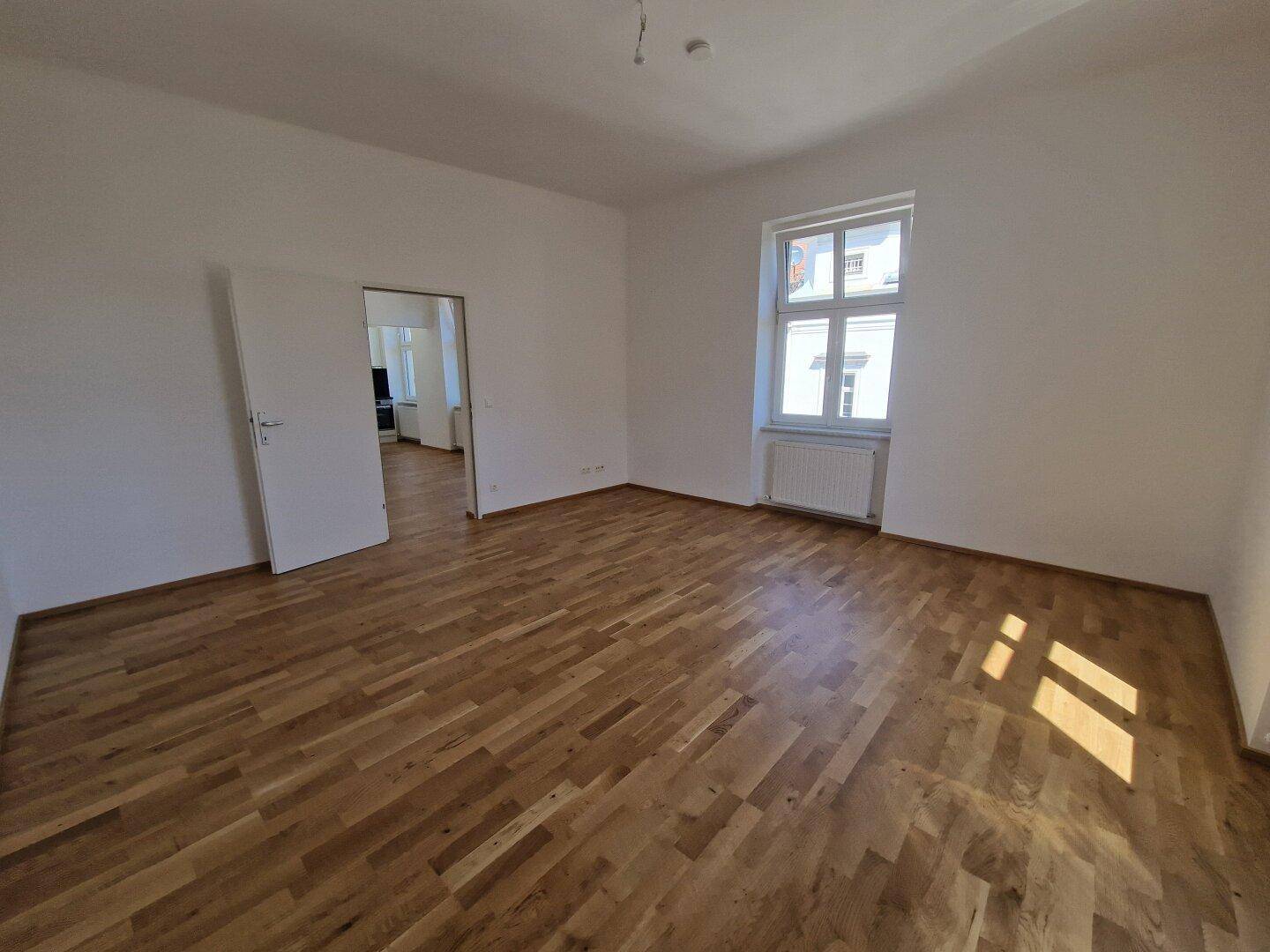 Helles, leeres Zimmer mit neuem Parkettboden und weiß gestrichenen Wänden, bereit zum Einzug.