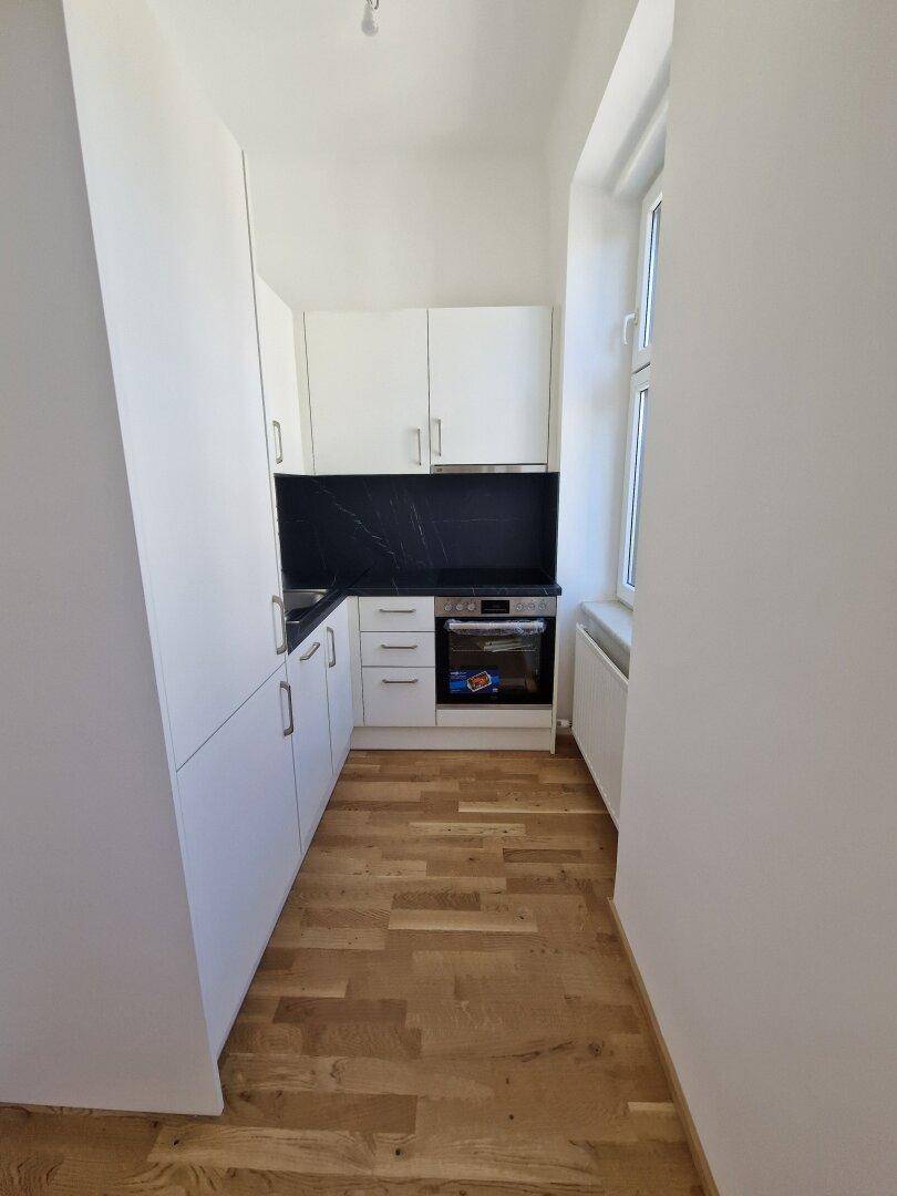 Schmale, moderne Küche mit weißen Schränken, dunkler Arbeitsplatte und integriertem Backofen.