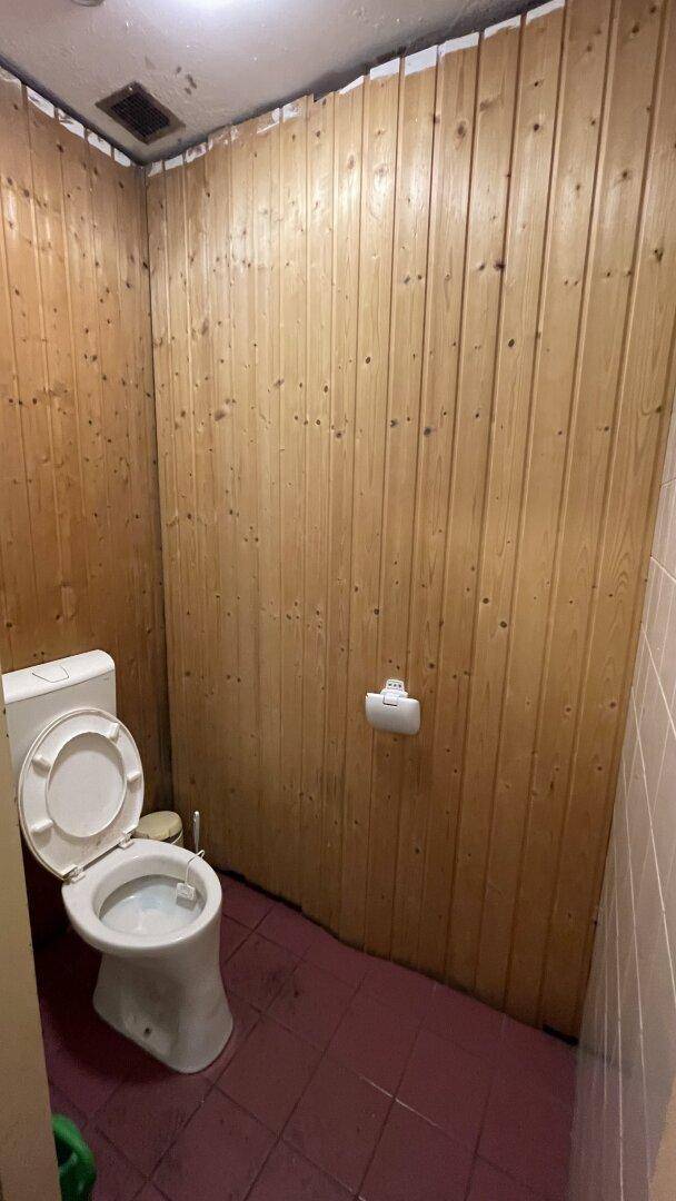 Toilettenkabine mit Holzvertäfelung und einer einfachen Toilette, roter Fliesenboden.