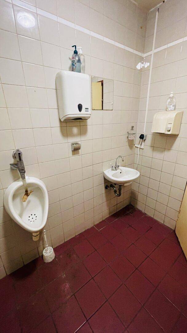 Badezimmer mit Urinal, Waschbecken und Fliesenwänden, roter Fliesenboden.