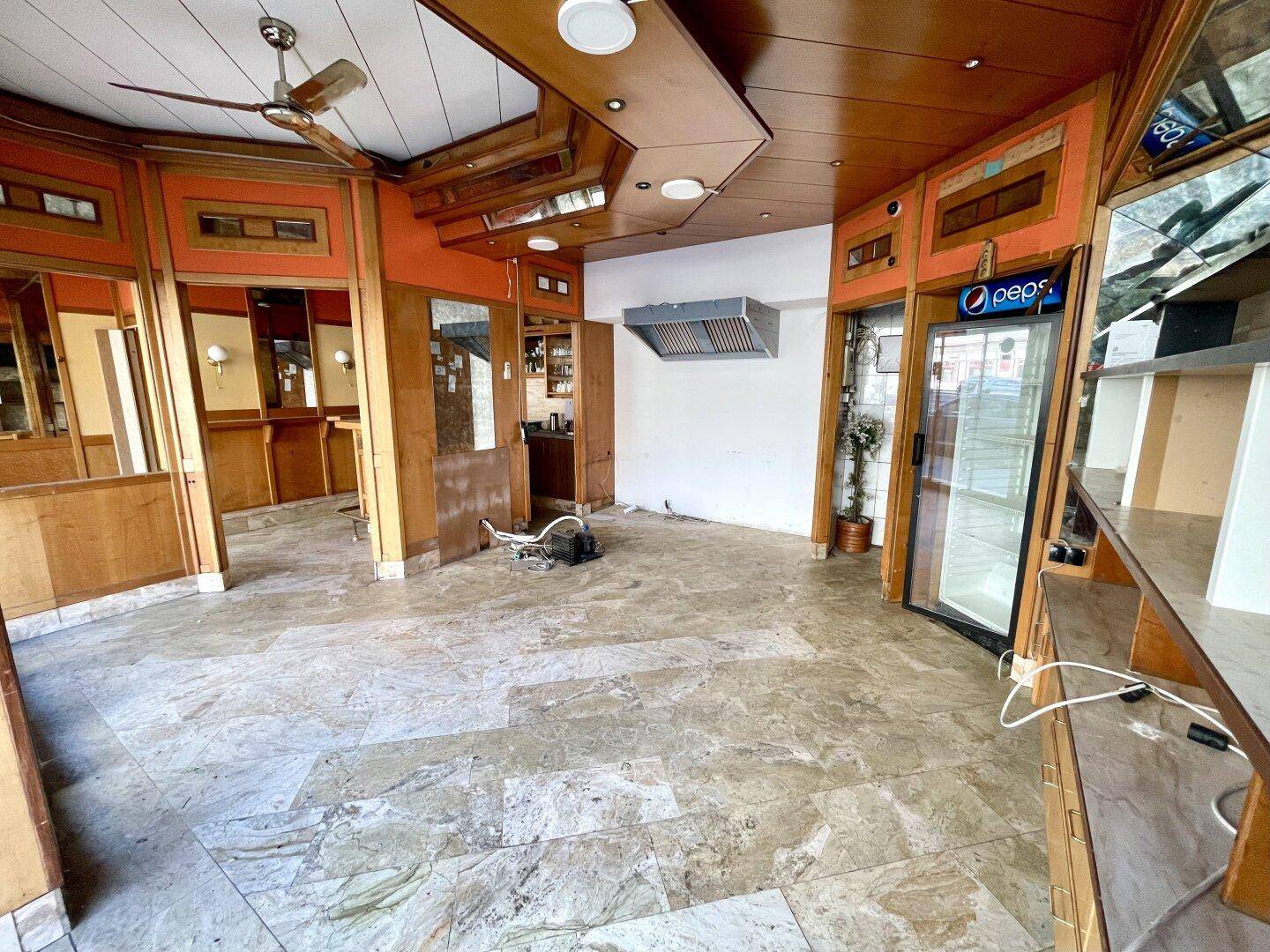 Verkaufsraum mit Marmorboden, Holzvertäfelung, Deckenventilator und einem leeren Getränkekühlschrank.