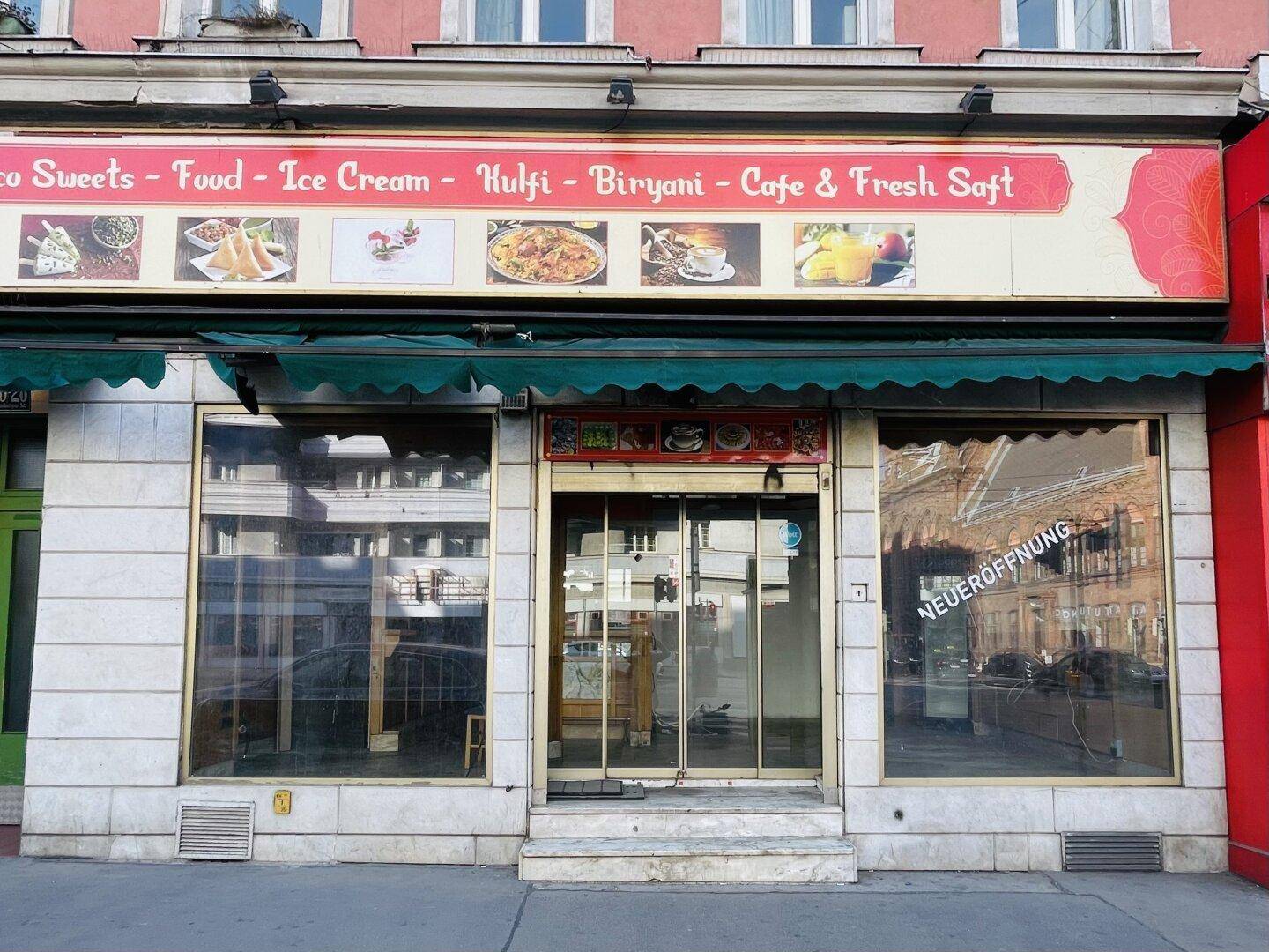 Schaufenster eines Ladengeschäfts im Erdgeschoss mit Werbeschildern und "Neueröffnung"-Hinweis.
