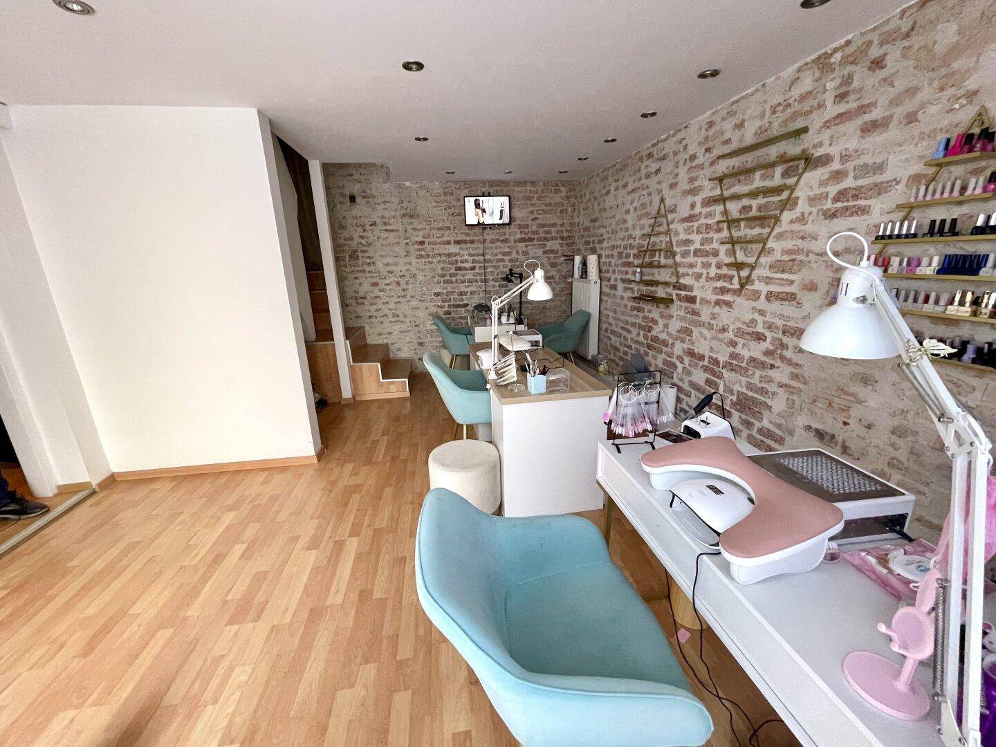 Blick in den Nagelstudio-Bereich mit Arbeitsplätzen, Ziegelwand und einer Treppe im Hintergrund.