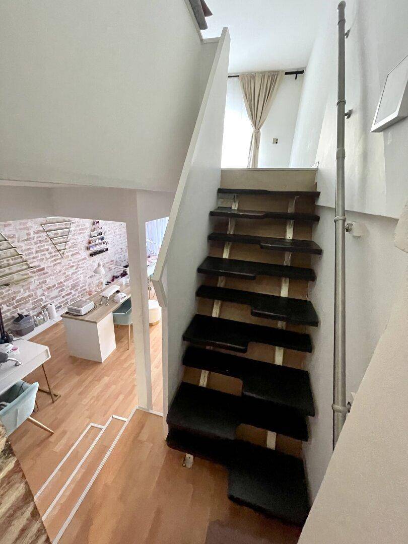 Moderne Treppe mit dunklen Holzstufen, die zu einer oberen Etage führt, mit Blick auf den Salonbereich.