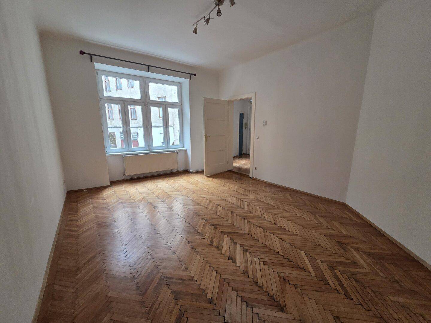 Geräumiges Zimmer mit klassischem Fischgrätparkett und Blick auf die umliegenden Gebäude.