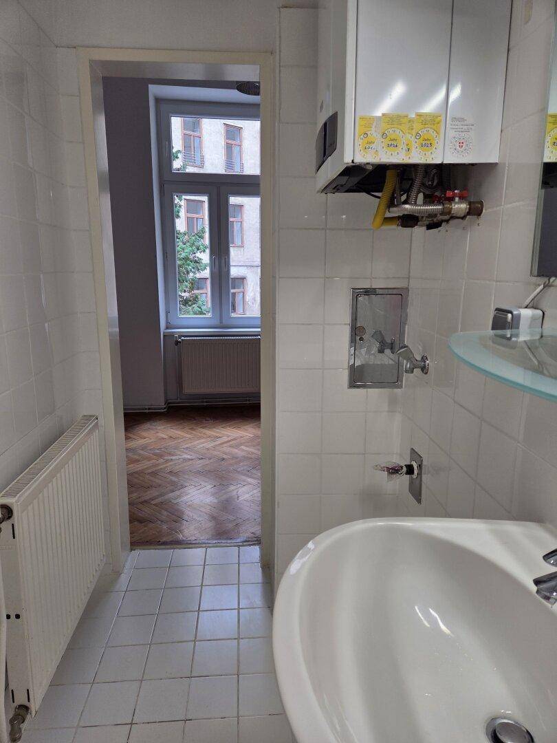 Badezimmer mit weißen Fliesen und Blick in einen angrenzenden Raum mit Parkettboden.