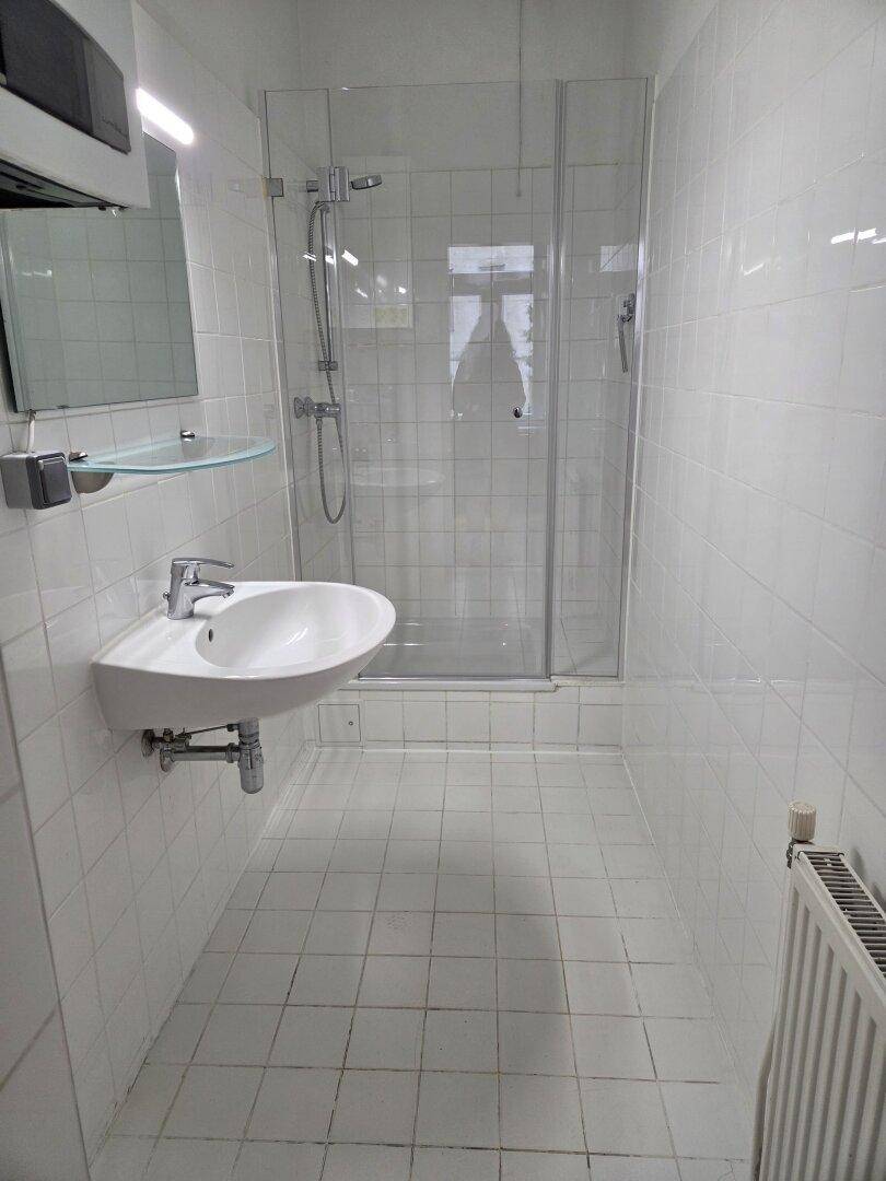 Modernes Badezimmer mit Duschkabine, Waschbecken und weißen Wand- und Bodenfliesen.