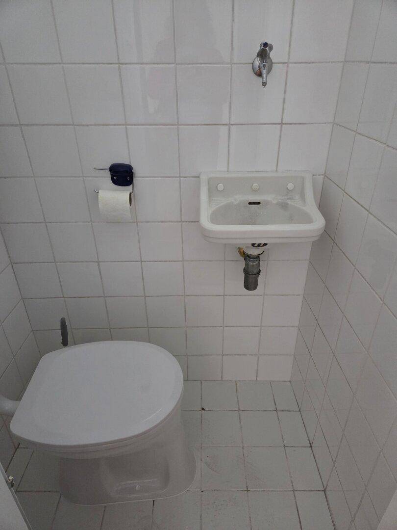 Kleines separates WC mit Waschbecken und weißen Fliesen, funktional und sauber.