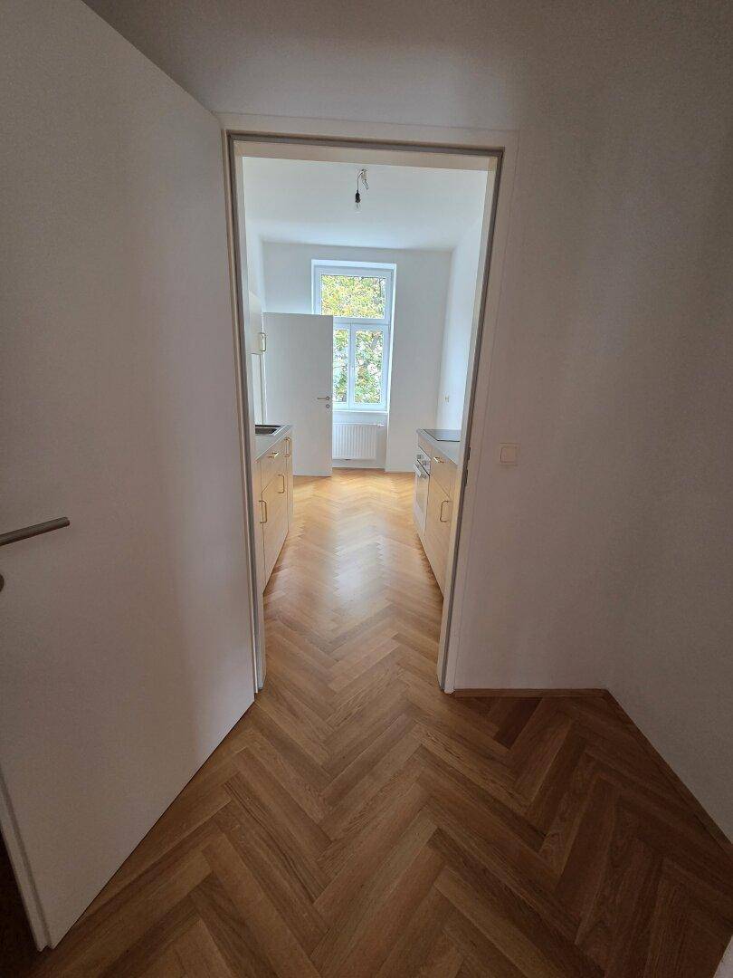 Heller Flur mit Fischgrätparkett, der in eine moderne Küche führt.
