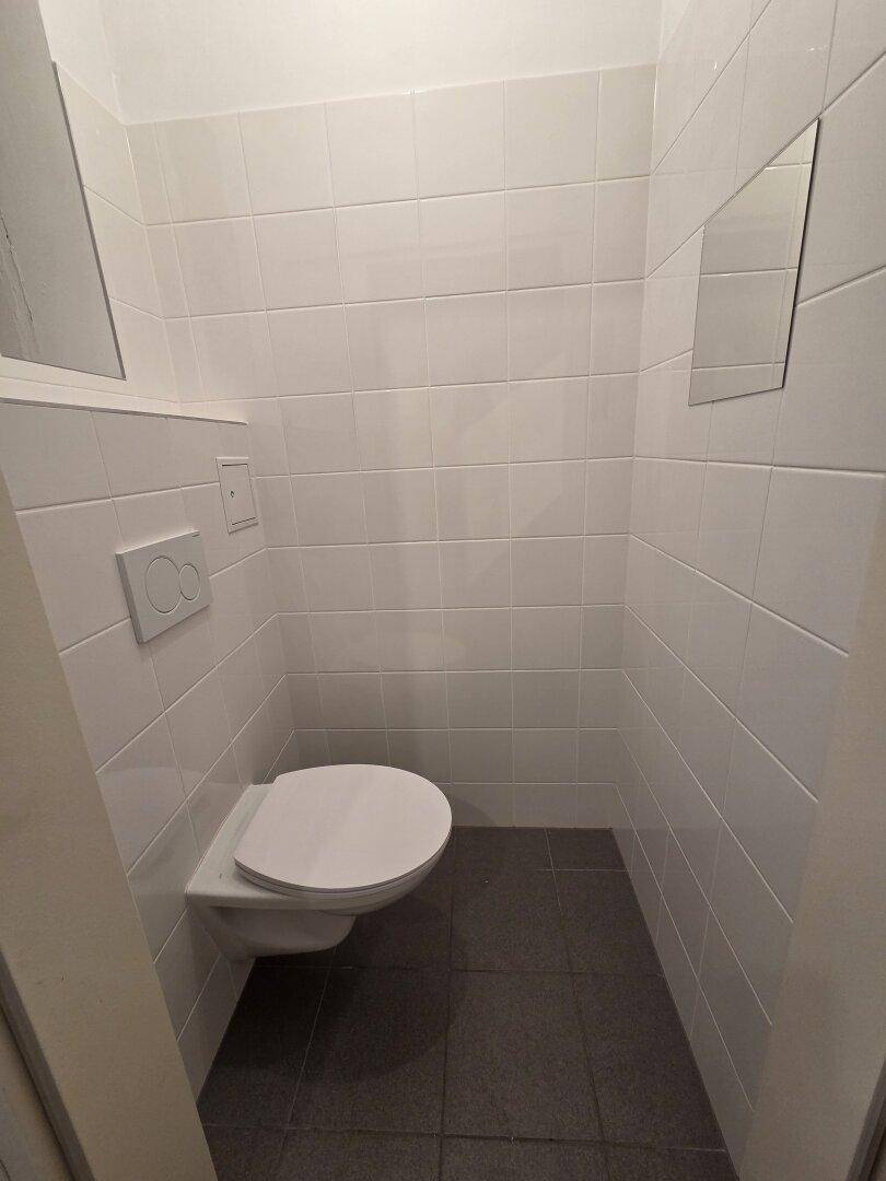 Separates WC mit wandhängender Toilette und weißen Fliesen.