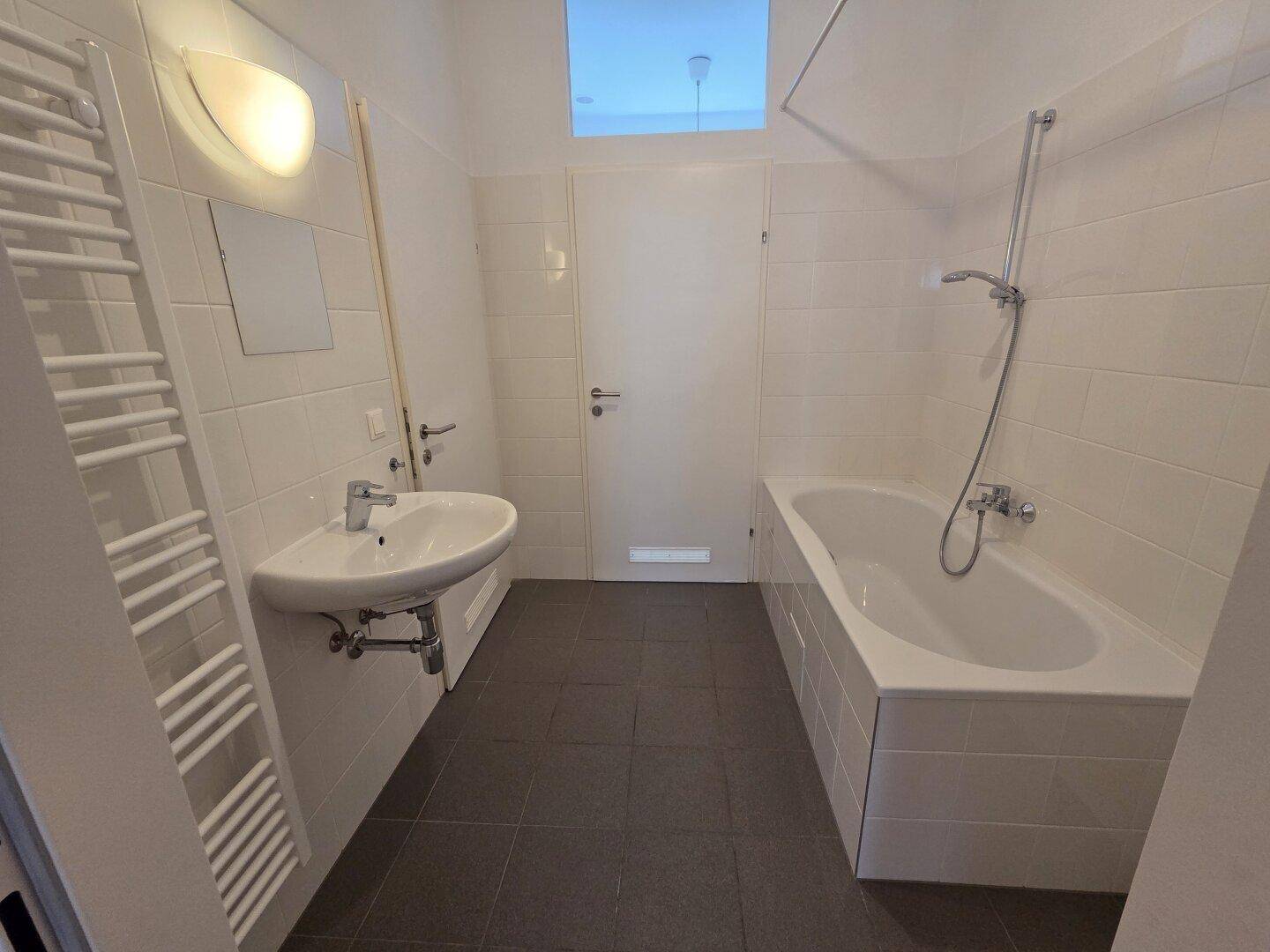 Gefliestes Badezimmer mit Badewanne, Waschbecken und beheiztem Handtuchhalter.