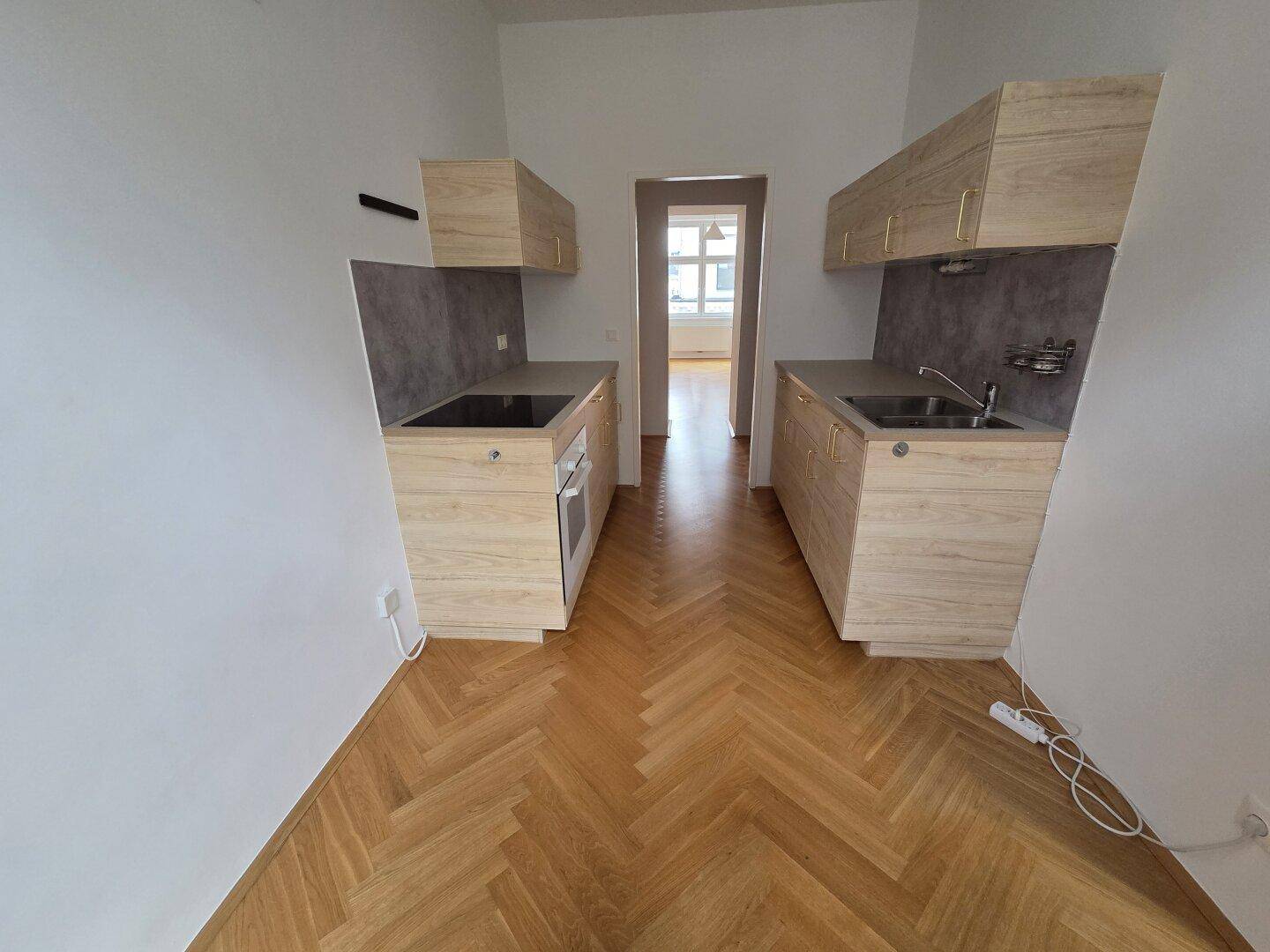 Moderne Küchenzeile mit Holzfronten und dunkler Arbeitsplatte, offen zum Flur.