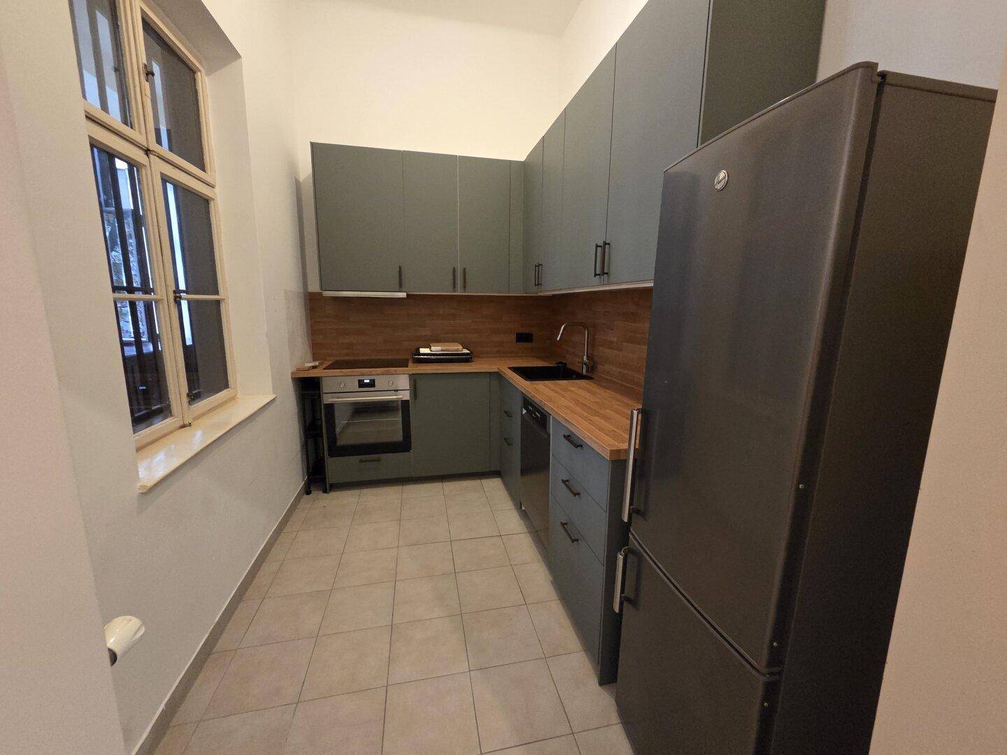Moderne Küche mit grauen Schränken, Holzarbeitsplatten und integrierten Geräten, inklusive Kühlschrank.
